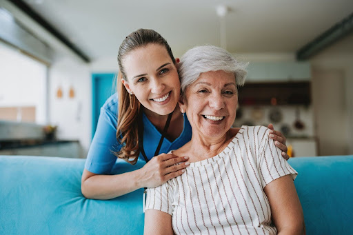 caregiver and senior lady smiling by blue couch