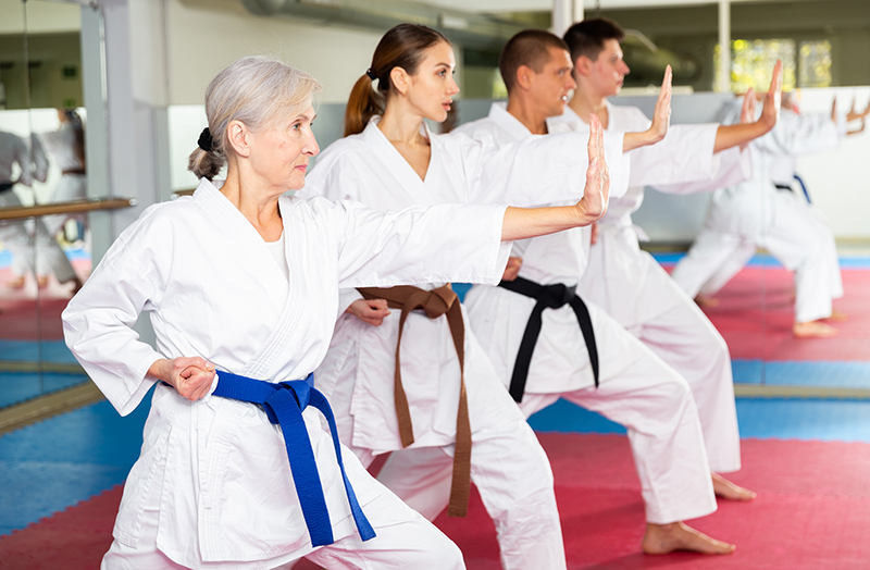 People of different ages standing in row and performing kata moves in gym during karate training.