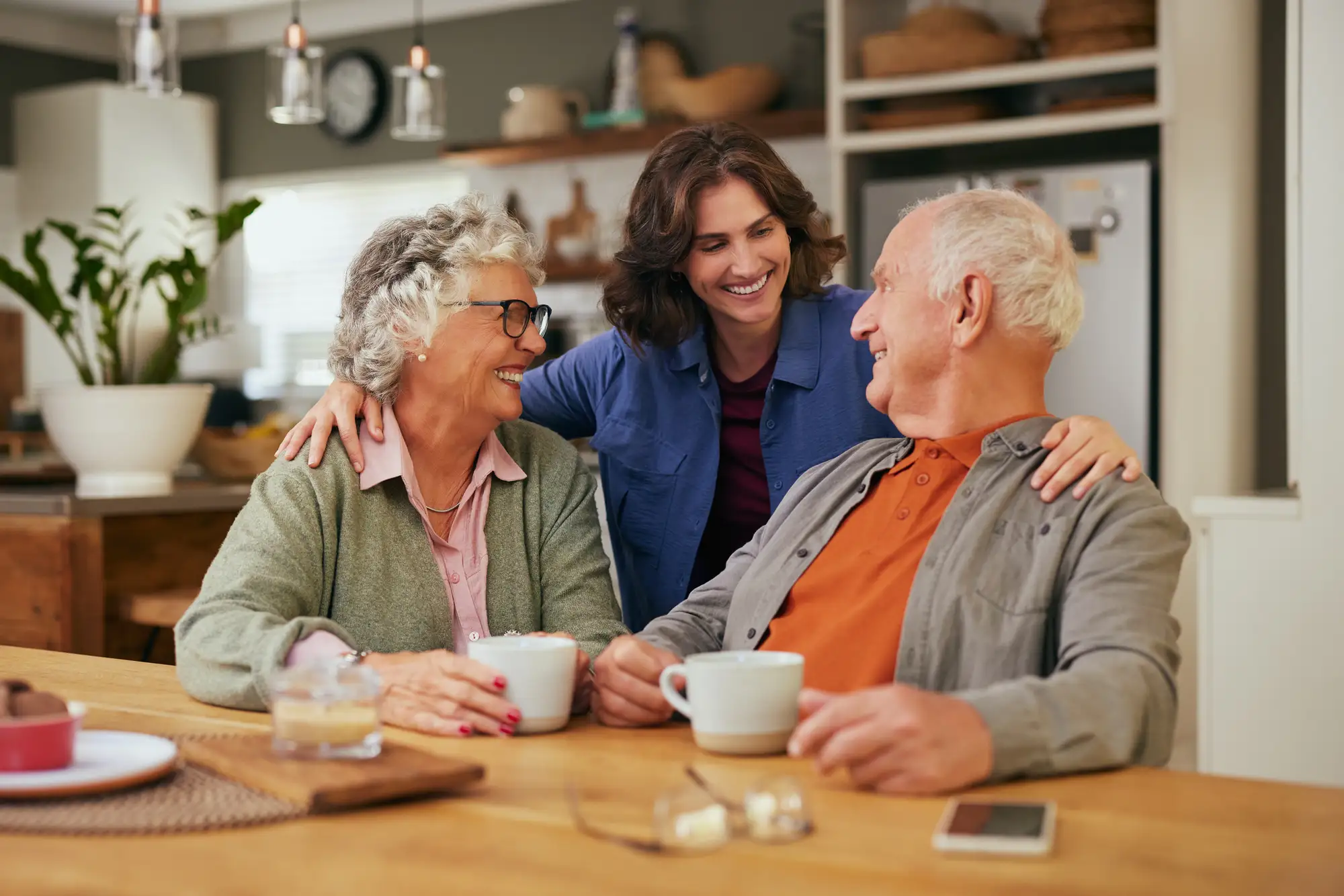 Elderly couple with adult daughter, smiling around a kitchen table while talking about independent living for seniors at Brandon Wilde in Augusta, GA.