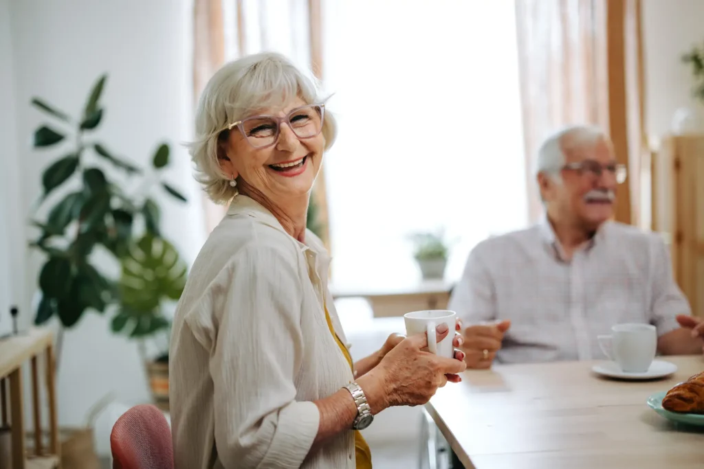 An elderly couple sitting at a table, smiling at the camera in their home at Brandon Wilde, an independent living community for seniors in Augusta, GA.